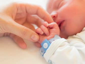 Mutter hält die Hand ihres neugeborenen Babys, das ein Namensbändchen am Handgelenk trägt. Mutter hält die Hand ihres neugeborenen Babys, das ein Namensbändchen am Handgelenk trägt.