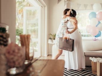 Frau übergibt bei der Begrüßung das Babyshower-Geschenk an die schwangere Gastgeberin. Frau übergibt bei der Begrüßung das Babyshower-Geschenk an die schwangere Gastgeberin.