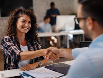 Vorbereitung Vorstellungsgespräch: Junge Frau wird von Recruiter begrüßt. Vorbereitung Vorstellungsgespräch: Junge Frau wird von Recruiter begrüßt.