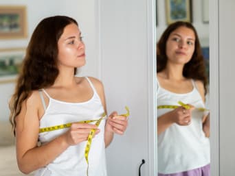 How to measure for a bra: a young woman standing in front of a mirror with a tape measure. How to measure for a bra: a young woman standing in front of a mirror with a tape measure.