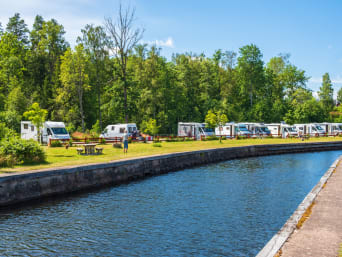 Campingurlaub planen: Wohnmobile stehen auf einem Campingplatz in der Nähe eines Kanals.