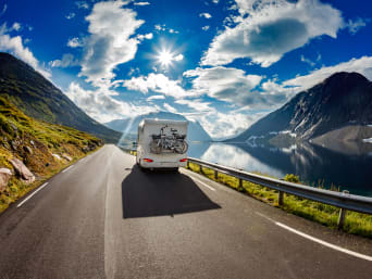 Camping-Tipps: Wohnmobil fährt auf einer Straße entlang eines Gebirgssees.