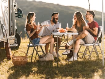 Camping für Anfänger – eine Gruppe Freunde unterhält sich auf dem Campingplatz.