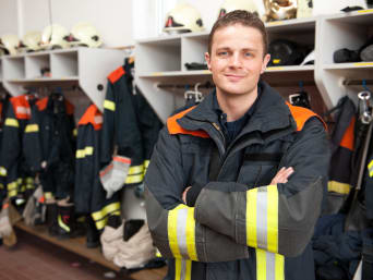 Ehrenamt Feuerwehr: Feuerwehrmann steht in der Umkleide mit Schutzkleidung.  Ehrenamt Feuerwehr: Feuerwehrmann steht in der Umkleide mit Schutzkleidung.