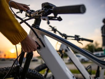 Frau schließt ihr E-Bike an eine Ladestation an. Frau schließt ihr E-Bike an eine Ladestation an.