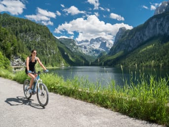 Radtouren Oberösterreich: Frau fährt auf einem Radweg am See mit Blick auf Dachsteingletscher Radtouren Oberösterreich: Frau fährt auf einem Radweg am See mit Blick auf Dachsteingletscher