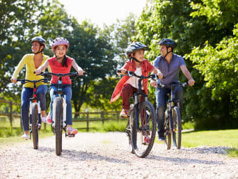 Velotouren Zürich: Junge Familie fährt mit dem Velo durch einen Park. Velotouren Zürich: Junge Familie fährt mit dem Velo durch einen Park.