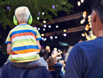 Festival met kinderen: jongetje met kindergehoorbescherming zit op de schouders van zijn vader. Festival met kinderen: jongetje met kindergehoorbescherming zit op de schouders van zijn vader.