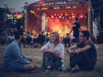 Welche Festivals gibt es? – Eine Gruppe von Freunden sitzt etwas abseits von der Festival-Bühne. Welche Festivals gibt es? – Eine Gruppe von Freunden sitzt etwas abseits von der Festival-Bühne.