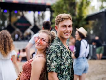 Men’s colourful festival outfits: a couple standing in front of a stage at a festival. Men’s colourful festival outfits: a couple standing in front of a stage at a festival.