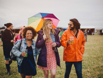 Festival outfit regen: vrienden lopen in regenkleding over het festivalterrein. Festival outfit regen: vrienden lopen in regenkleding over het festivalterrein.