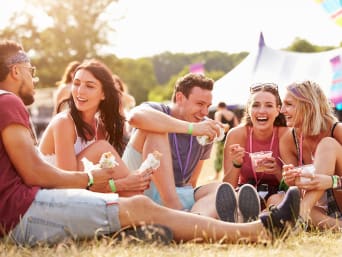 Festivalgids: vrienden zitten samen aan een maaltijd op de festivalweide. Festivalgids: vrienden zitten samen aan een maaltijd op de festivalweide.