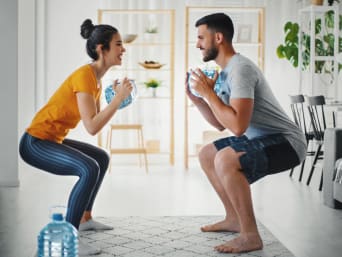 Two athletes are using water bottles as weights for full-body training at home. Two athletes are using water bottles as weights for full-body training at home.
