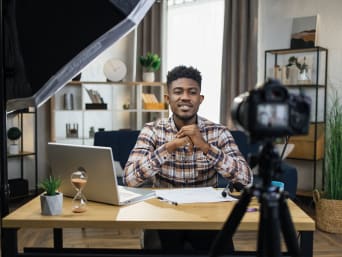 Making videos – a man sitting in front of a camera at his desk.  Making videos – a man sitting in front of a camera at his desk.