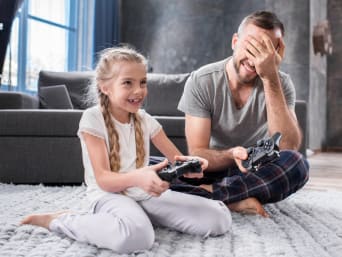 Hoe lang mogen kinderen gamen? Vader helpt dochter bij het gamen. Hoe lang mogen kinderen gamen? Vader helpt dochter bij het gamen.