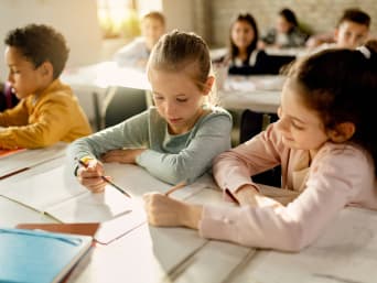 Kompetenzen Grundschule – Schülerin hilft einer Klassenkameradin im Unterricht Kompetenzen Grundschule – Schülerin hilft einer Klassenkameradin im Unterricht