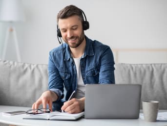 Sprachen lernen: Junger Mann sitzt auf dem Sofa und lernt mit Headset eine neue Sprache. Sprachen lernen: Junger Mann sitzt auf dem Sofa und lernt mit Headset eine neue Sprache.