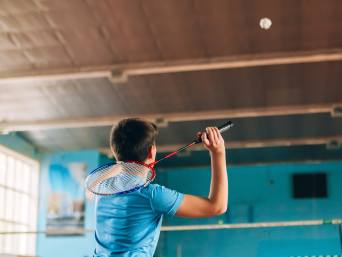 Badminton Übungen für Kinder: Ein Junge spielt einen Federball über das Netz zurück. Badminton Übungen für Kinder: Ein Junge spielt einen Federball über das Netz zurück.