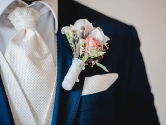 Outfits for a registry office wedding: a groom wearing a patterned tie with a thick tie knot and a flower pin. Outfits for a registry office wedding: a groom wearing a patterned tie with a thick tie knot and a flower pin.