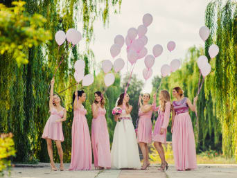 Wedding guest outfits for women: a bride and her bridesmaids in pink dresses letting go of some balloons. Wedding guest outfits for women: a bride and her bridesmaids in pink dresses letting go of some balloons.