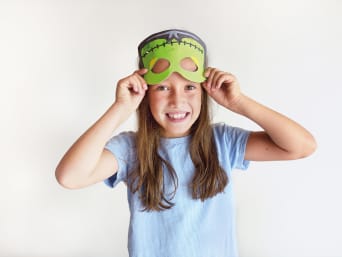 Faschingsmaske basteln mit Kindern: Mädchen zieht eine selbstgebastelte Maske auf. Faschingsmaske basteln mit Kindern: Mädchen zieht eine selbstgebastelte Maske auf.