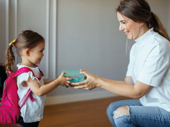 Kindergarten Checkliste: Mutter gibt ihrer Tochter die Brotdose für den Kindergarten.