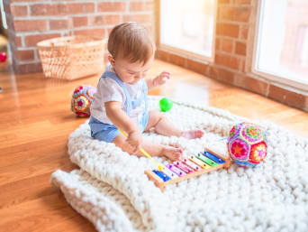 Geschenk für 2-Jährige: Kleinkind sitzt auf dem Boden und spielt auf einem Xylophon. Geschenk für 2-Jährige: Kleinkind sitzt auf dem Boden und spielt auf einem Xylophon.