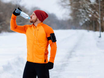 Going for a winter run: a runner taking a break and drinking water. Going for a winter run: a runner taking a break and drinking water.