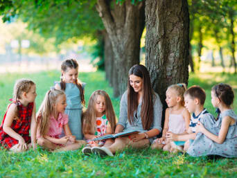 Leren lezen op de basisschool: leerkracht leest met kinderen in het park. Leren lezen op de basisschool: leerkracht leest met kinderen in het park.