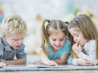 Spielerisch lesen lernen: Kleinkinder schauen ein Bilderbuch an. Spielerisch lesen lernen: Kleinkinder schauen ein Bilderbuch an.