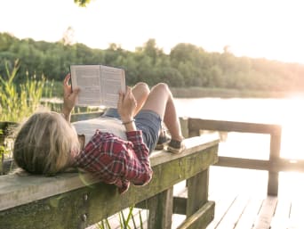 Lesemotivation fördern: Mädchen liest ihr Buch bei schönem Wetter draußen am See. Lesemotivation fördern: Mädchen liest ihr Buch bei schönem Wetter draußen am See.