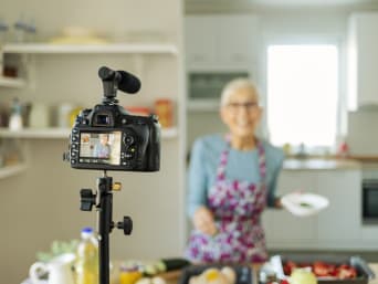 Senioren online – Seniorin steht vor der Kamera und dreht ein Kochvideo. Senioren online – Seniorin steht vor der Kamera und dreht ein Kochvideo.