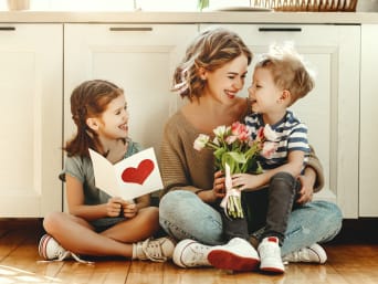 Twee kleine kinderen feliciteren hun moeder met een kaart en een boeket bloemen.