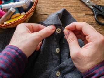Repairing old clothes: a man is sewing a button back onto his shirt. Repairing old clothes: a man is sewing a button back onto his shirt.