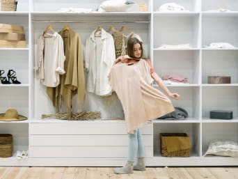 How to build a capsule wardrobe: a woman looking through her clothes in her wardrobe. How to build a capsule wardrobe: a woman looking through her clothes in her wardrobe.