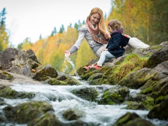 Mutter und Tochter sitzen an einem Bach im Wald und hören dem rauschenden Wasser zu. Mutter und Tochter sitzen an einem Bach im Wald und hören dem rauschenden Wasser zu.