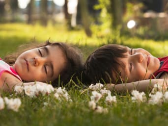 Zwei Kinder liegen mit geschlossenen Augen auf einer Wiese und lauschen den Klängen der Natur. Zwei Kinder liegen mit geschlossenen Augen auf einer Wiese und lauschen den Klängen der Natur.