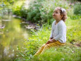 Kleines Mädchen sitzt mit geschlossenen Augen an einem Fluss und hört das Wasser plätschern. Kleines Mädchen sitzt mit geschlossenen Augen an einem Fluss und hört das Wasser plätschern.