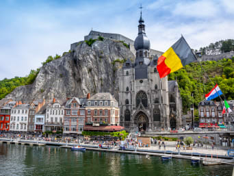 De historische stad Dinant met de Belgische vlag en de citadel op de rots en de collegiale kerk Notre-Dame aan de Maas. De historische stad Dinant met de Belgische vlag en de citadel op de rots en de collegiale kerk Notre-Dame aan de Maas.