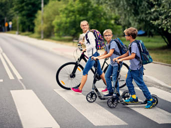Schulweg mit Fahrrad: Eine Gruppe Kinder fährt mit Tretrollern und mit dem Fahrrad zur Schule. Schulweg mit Fahrrad: Eine Gruppe Kinder fährt mit Tretrollern und mit dem Fahrrad zur Schule.