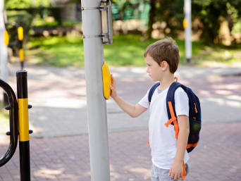 Lopend naar school: Kleine jongen wacht bij een verkeerslicht.