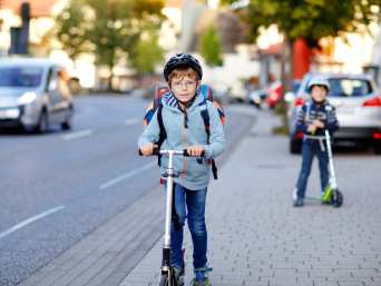 Mit dem Roller zur Schule: Zwei Volksschüler fahren mit dem Roller auf dem Gehweg.  Mit dem Roller zur Schule: Zwei Volksschüler fahren mit dem Roller auf dem Gehweg.