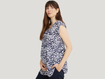 What to wear during pregnancy: a woman in the first trimester covering up her baby bump with a loose-fitting top. What to wear during pregnancy: a woman in the first trimester covering up her baby bump with a loose-fitting top.
