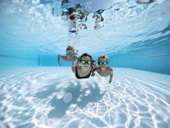 Richtiges Verhalten im Schwimmbad: Drei Kinder mit Schwimmbrillen tauchen im Schwimmbecken. Richtiges Verhalten im Schwimmbad: Drei Kinder mit Schwimmbrillen tauchen im Schwimmbecken.
