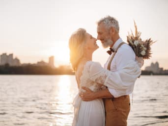 Kleidung für Silberhochzeit: Älteres Ehepaar in festlicher Kleidung umarmt sich am Strand.