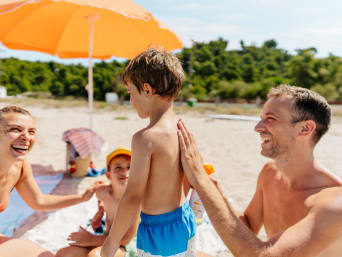 Kinder Sonnenschutz: Vater hilft seinem Kind beim Eincremen am Strand. Kinder Sonnenschutz: Vater hilft seinem Kind beim Eincremen am Strand.