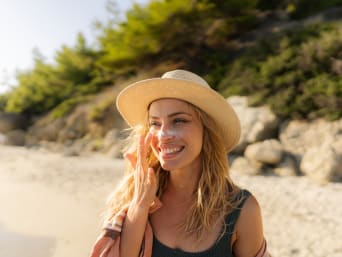 Junge Frau trägt Sonnencreme als Sonnenschutz am Strand auf.  Junge Frau trägt Sonnencreme als Sonnenschutz am Strand auf.