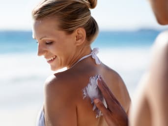 Sonnencreme als wichtiges Sonnenschutzmittel: Frau wird von ihrem Begleiter am Strand eingecremt. Sonnencreme als wichtiges Sonnenschutzmittel: Frau wird von ihrem Begleiter am Strand eingecremt.