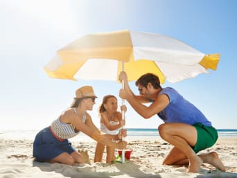 Sonnenschutz am Strand: Familie stellt einen Sonnenschirm auf. Sonnenschutz am Strand: Familie stellt einen Sonnenschirm auf.