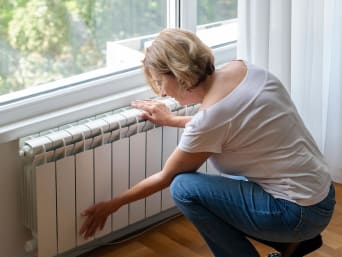 Duurzaam verwarmen – vrouw controleert of de radiator ontlucht moet worden. Duurzaam verwarmen – vrouw controleert of de radiator ontlucht moet worden.